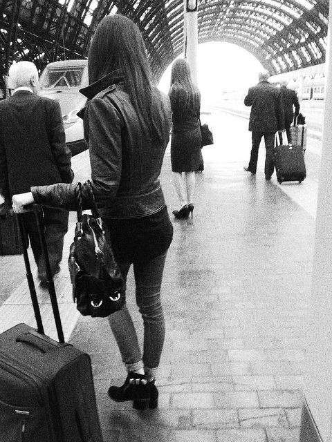 Ragazza con valigia aspetta il treno alla stazione centrale di Milano